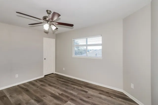 an empty room with wooden floor fan and windows