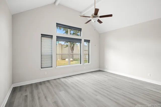 an empty room with wooden floor fan and windows