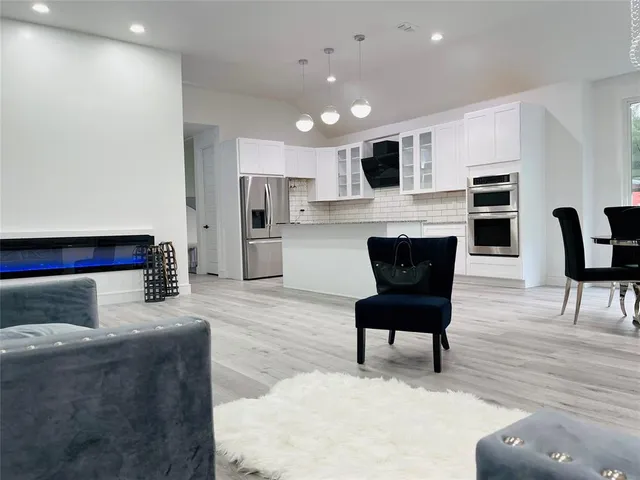 a living room with stainless steel appliances furniture a rug and a kitchen view