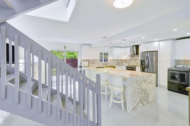 a kitchen with stainless steel appliances kitchen island granite countertop a refrigerator a stove a sink dishwasher and white cabinets with wooden floor