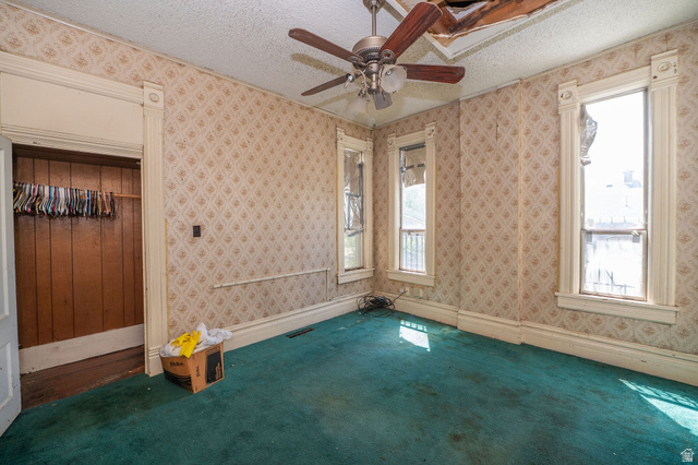 1256 24th Street Ogden, UT 84401 - Photo 14 of 34 Room featuring patterned wallpaper, significant window trim, an open closet with wood paneling, a ceiling fan, and teal carpeting