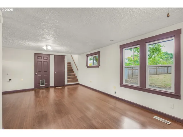 a view of an empty room with wooden floor and windows