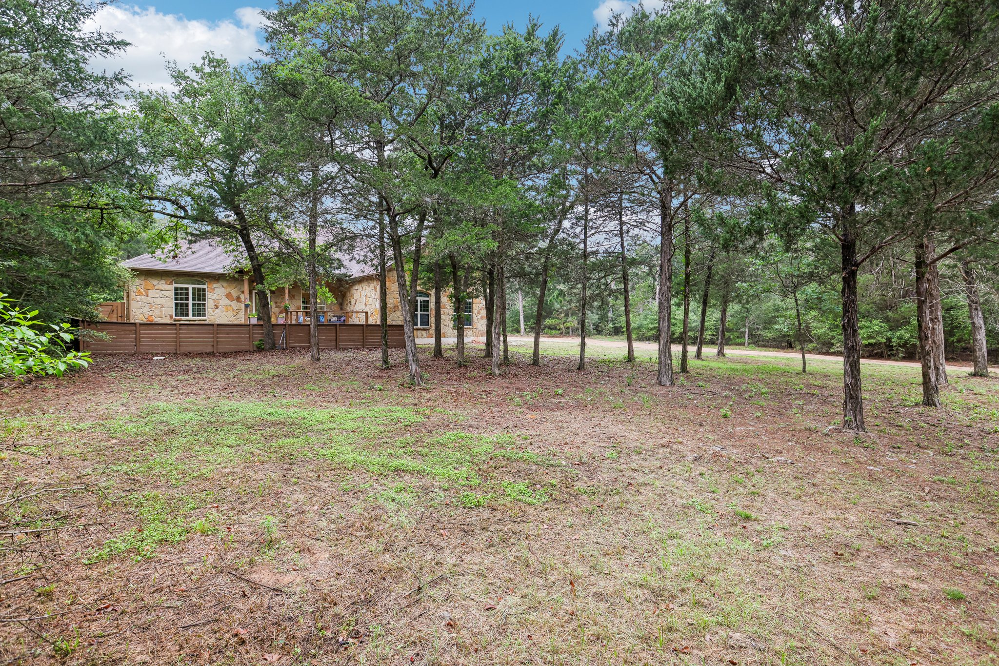 267 Corral Road Smithville, TX 78957 - Photo 7 of 40 Stone facade residence featuring a brown shingle roof and white-framed windows, partially obscured by mature trees