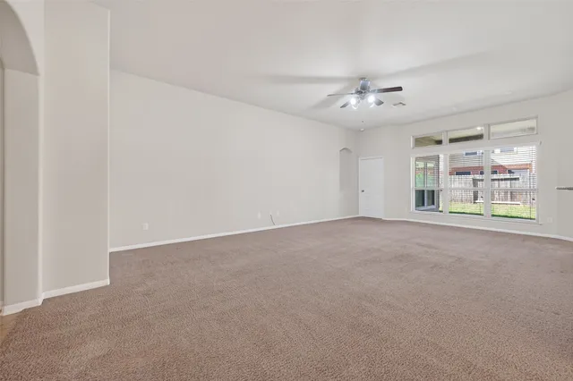 an empty room with chandelier fan and windows