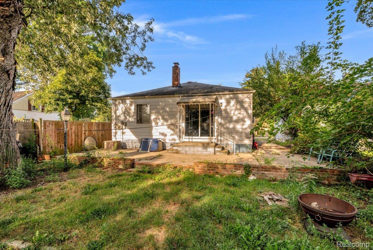 1215 Center Street Inkster, MI 48141 - Photo 27 of 30 Rear exterior featuring a brick chimney, a sliding glass door, and a concrete patio with a partial brick retaining wall