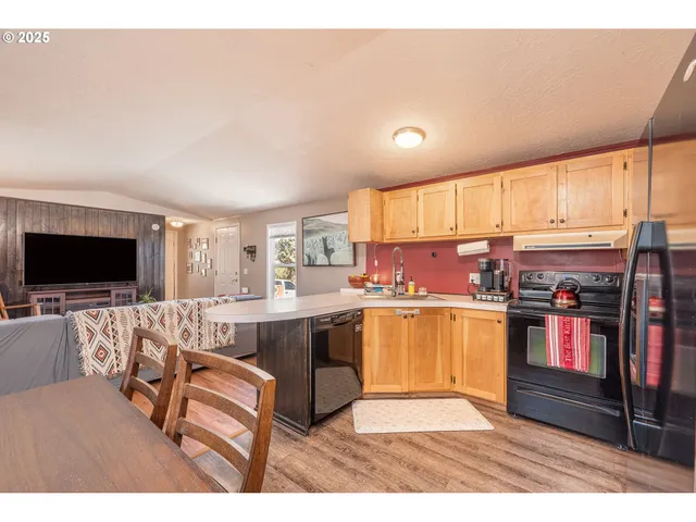 a living room with stainless steel appliances furniture a flat screen tv and kitchen view