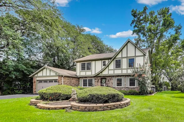 a house that is sitting in the grass with large trees and plants