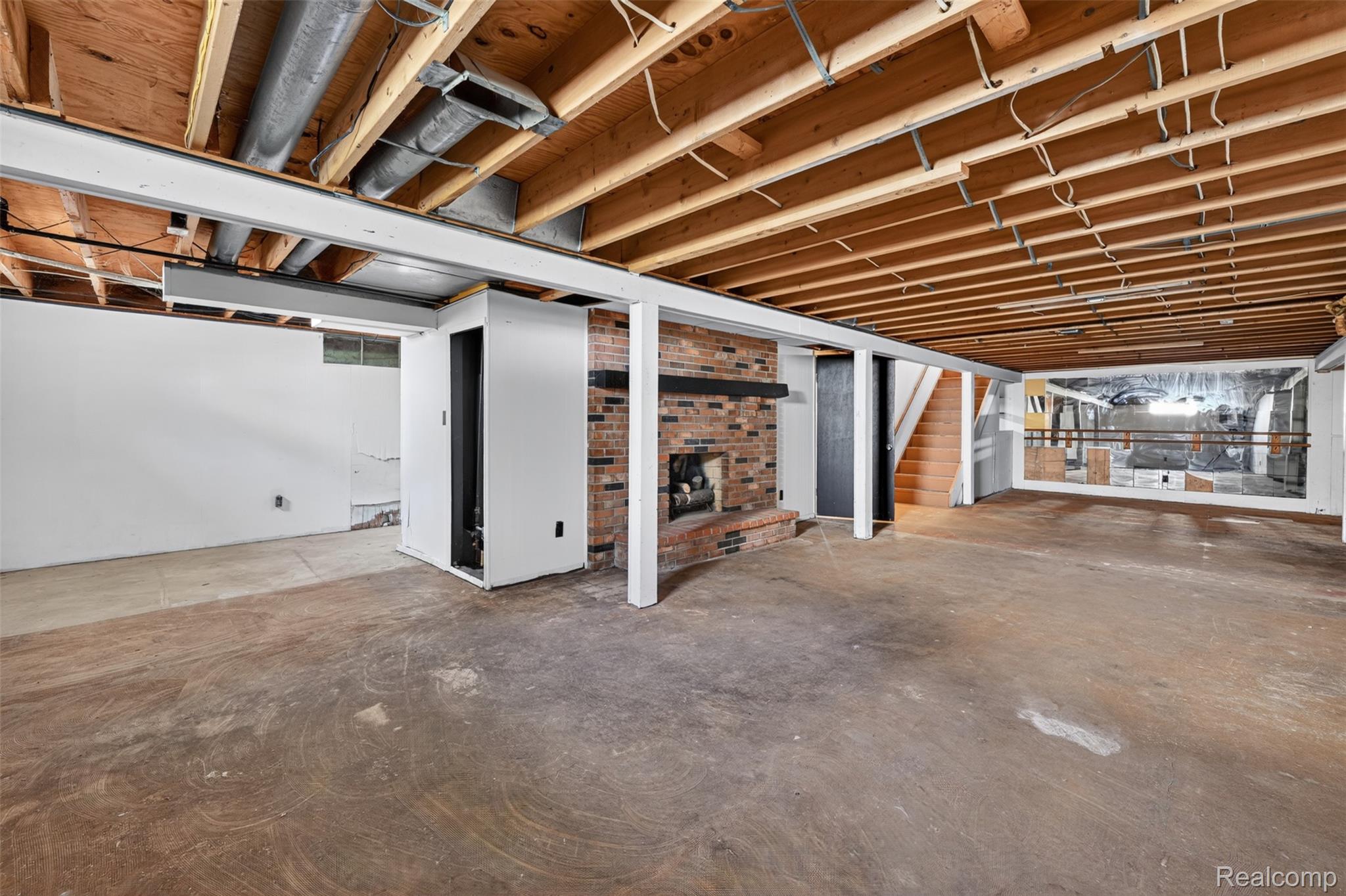 5457 Reid Road Swartz Creek, MI 48473 - Photo 36 of 51 Expansive unfinished basement featuring a prominent brick fireplace with a dark wood mantel, exposed ceiling joists, and a concrete floor