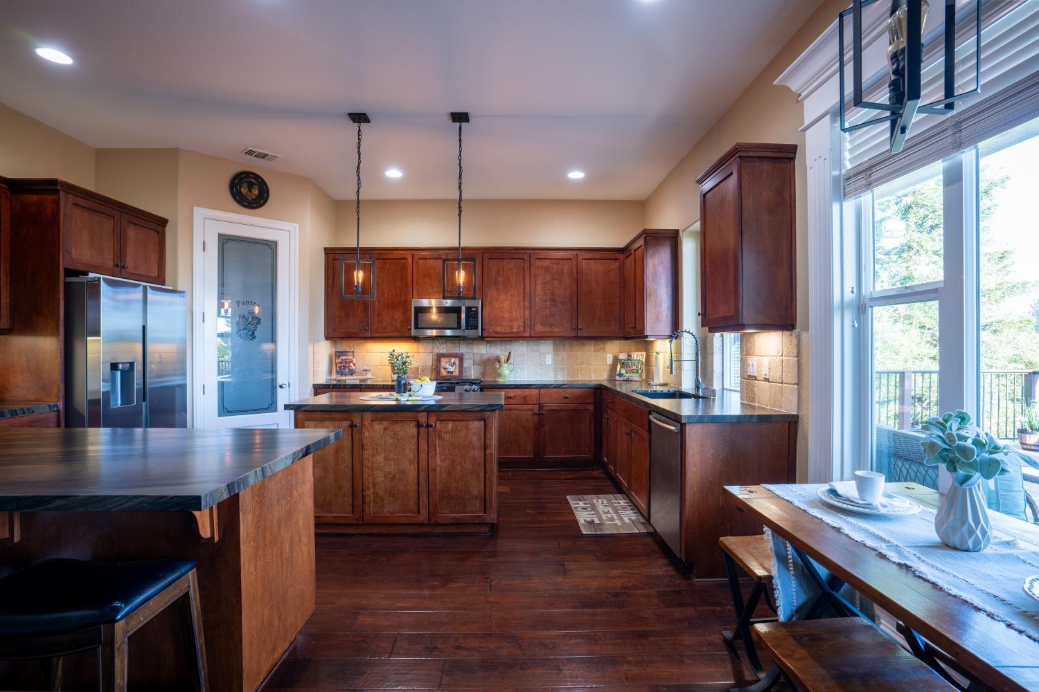3388 Sudbury Road Cameron Park, CA 95682 - Photo 8 of 47 a large kitchen with stainless steel appliances kitchen island granite countertop a large stove a refrigerator a sink a dining table and chairs with wooden floor