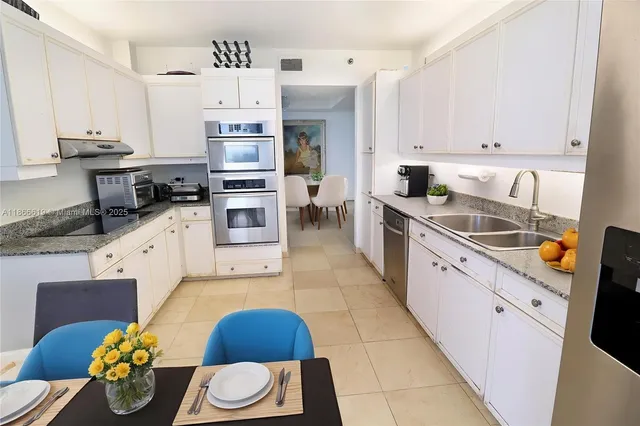 a large white kitchen with stainless steel appliances granite countertop a stove a sink a refrigerator and white cabinets