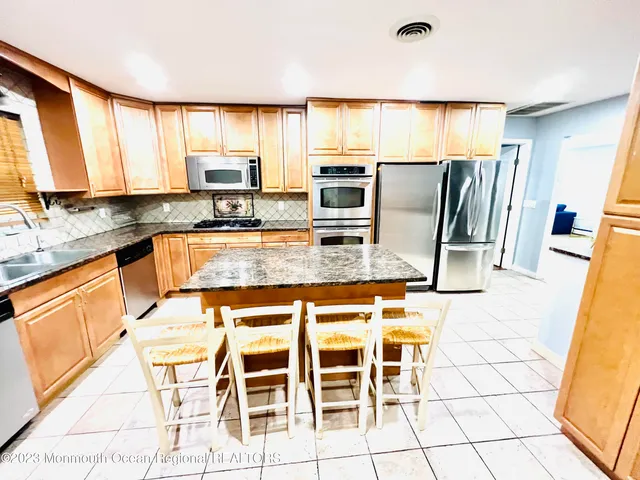 a kitchen with stainless steel appliances granite countertop a stove top oven a sink a dining table and chairs