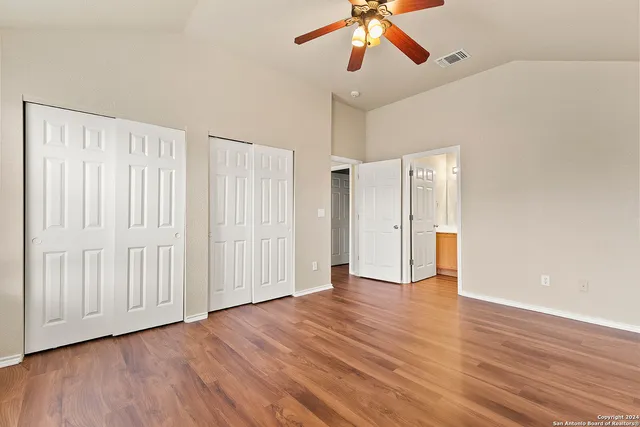 an empty room with wooden floor chandelier fan and windows