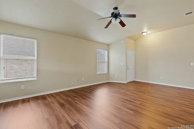 an empty room with wooden floor ceiling fan and window