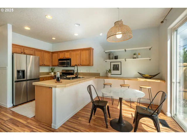 a kitchen with stainless steel appliances granite countertop a refrigerator a stove a sink dishwasher a dining table and chairs with wooden floor