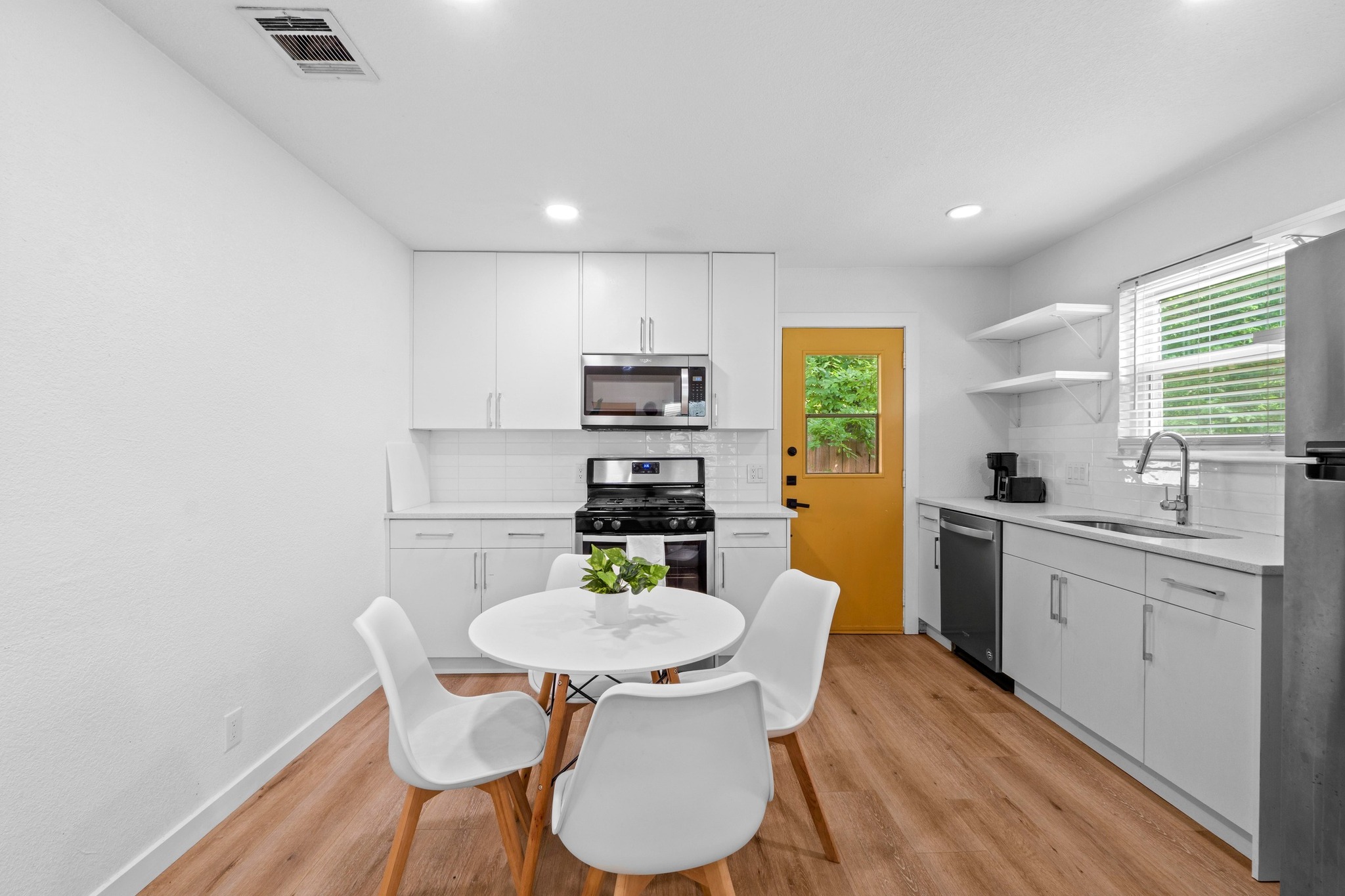 10601 Macmora Road, Unit B Austin, TX 78758 - Photo 7 of 22 A well-lit kitchen with sleek white cabinetry, wood flooring, and a cheerful yellow door.