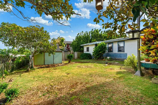 a backyard of a house with table and chairs plants and large tree
