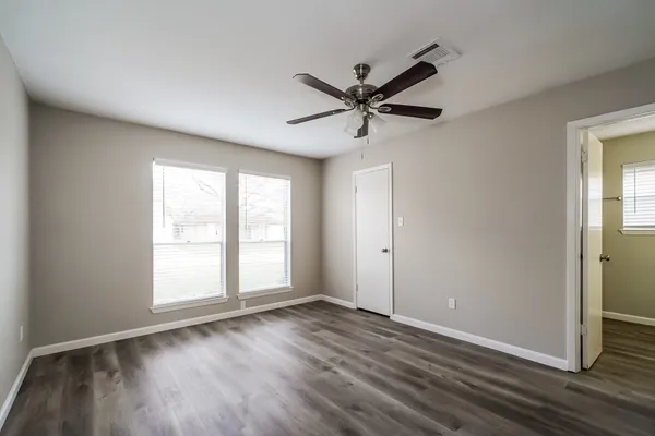 an empty room with wooden floor fan and windows