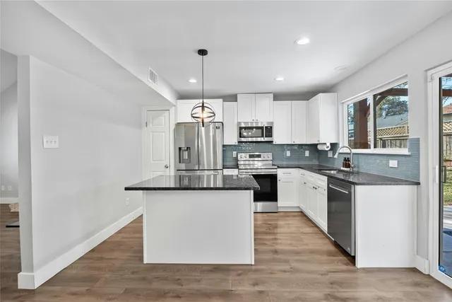 a kitchen with stainless steel appliances kitchen island granite countertop a stove top oven a sink dishwasher a refrigerator and white cabinets with wooden floor