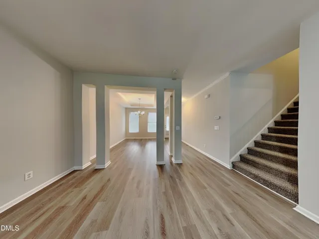 an empty room with wooden floor kitchen view and a window
