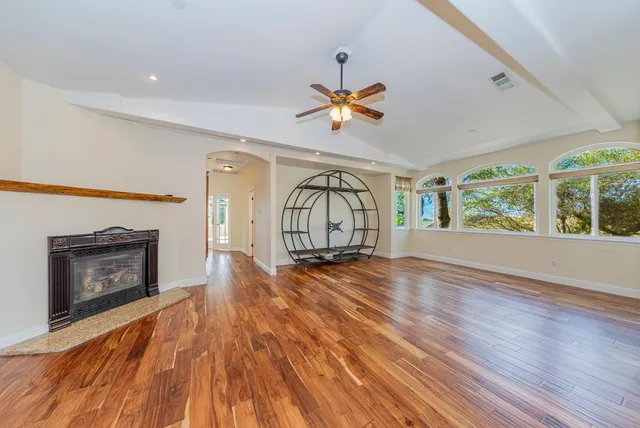 an empty room with wooden floor ceiling fan and windows