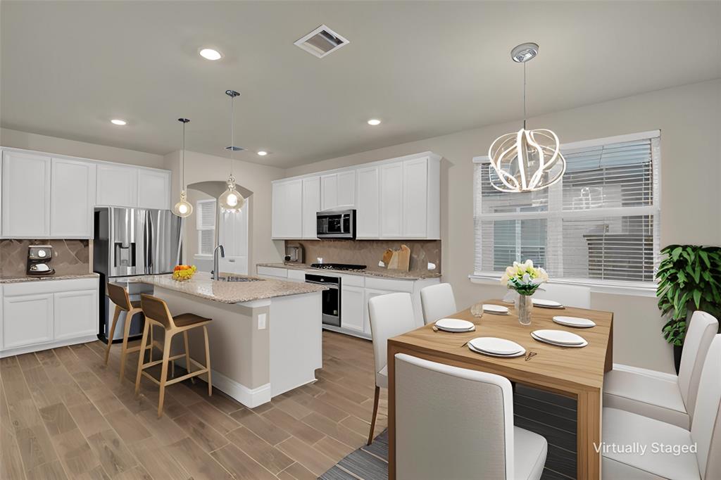 a kitchen that has a lot of cabinets in it with stainless steel appliances granite countertop a stove a sink a dining table and chairs with wooden floor