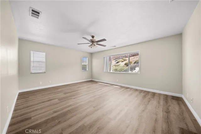 an empty room with wooden floor chandelier fan and windows
