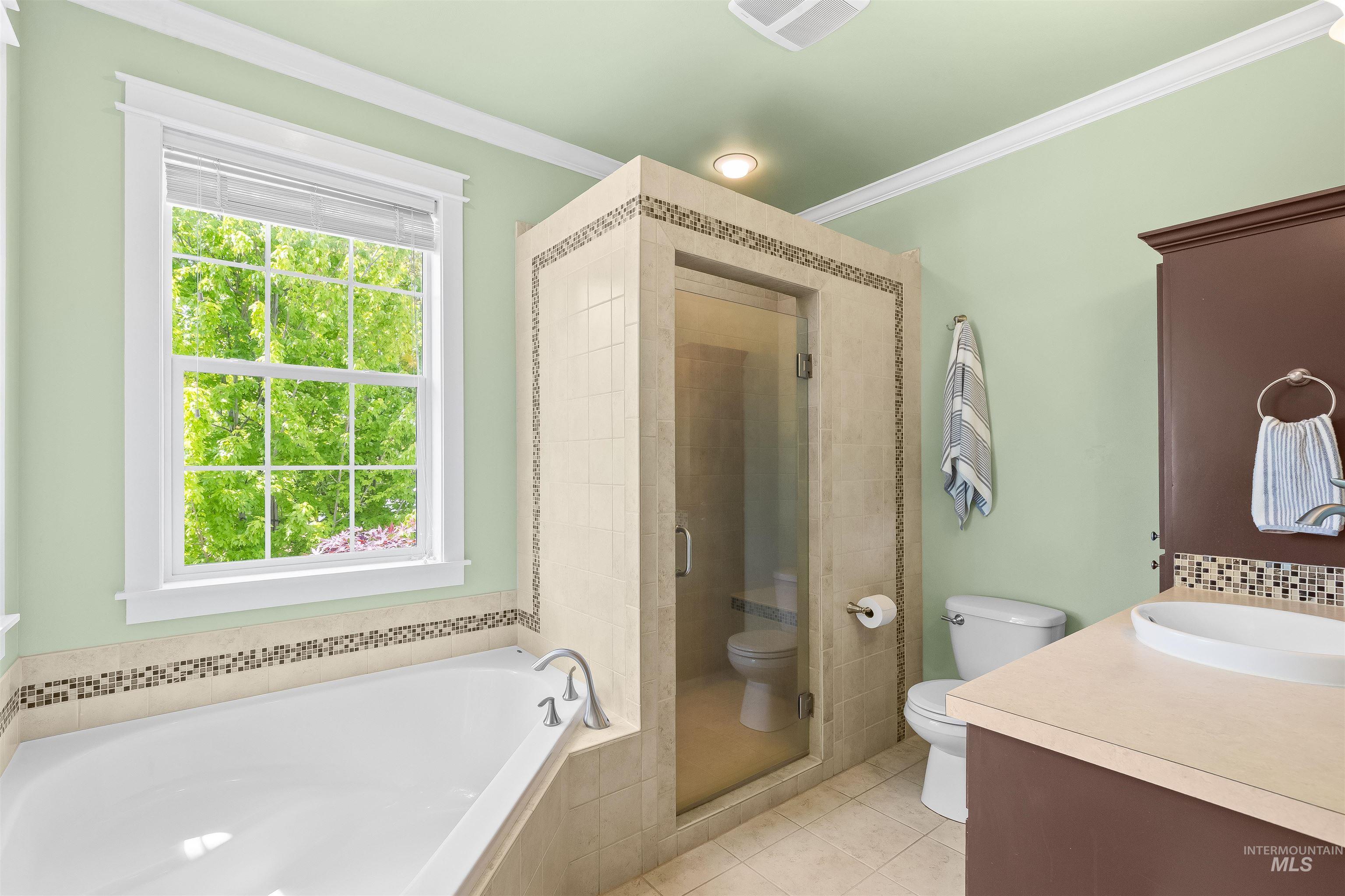 1617 Pine Cone Road Moscow, ID 83843 - Photo 22 of 44 Contemporary bathroom featuring a built-in soaking tub with a tiled surround, a glass-enclosed shower with decorative tile accents, a single-sink vanity with an oval basin, and crown molding
