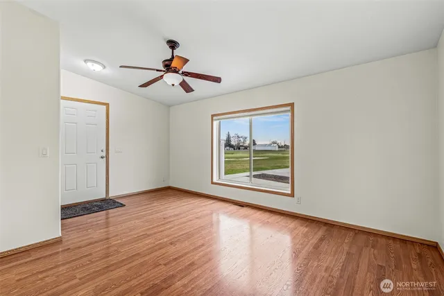 an empty room with wooden floor ceiling fan and windows