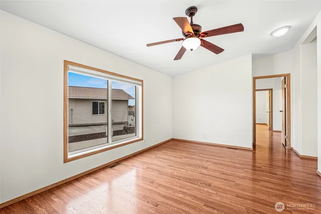 a view of an empty room with wooden floor and a ceiling fan