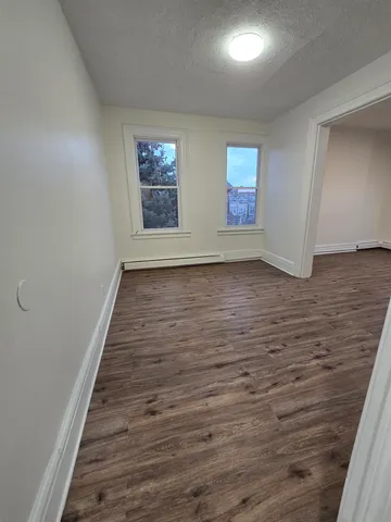 a view of an empty room with wooden floor and window