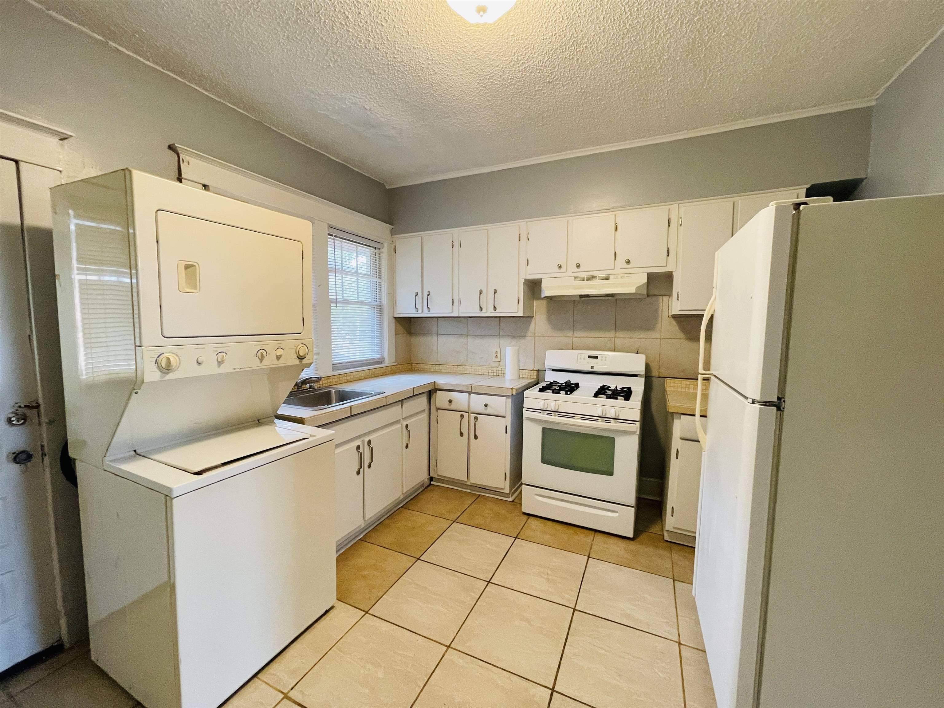1009 Rozelle Street Memphis, TN 38114 - Photo 31 of 40 Kitchen with backsplash, stacked washer and clothes dryer, white cabinetry, and white appliances