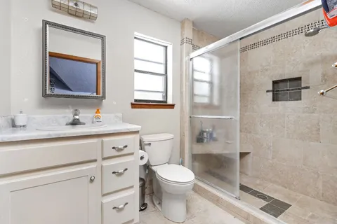 a bathroom with a toilet a sink a mirror a shower a vanity and window
