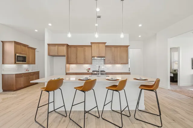 a kitchen with stainless steel appliances granite countertop a stove a sink a refrigerator and chairs with wooden floor