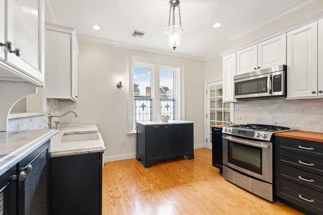 a kitchen with stainless steel appliances kitchen island granite countertop a stove top oven a sink a window and white cabinets