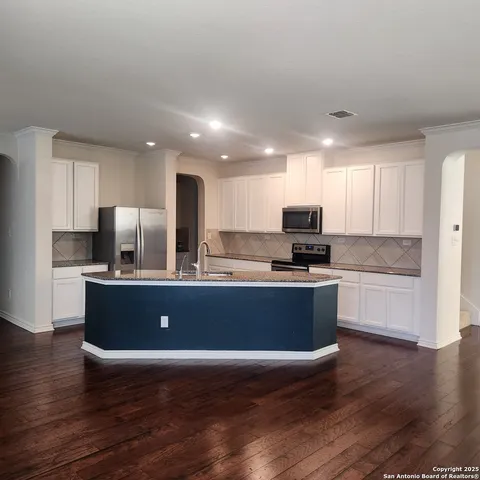 a kitchen with stainless steel appliances granite countertop a stove a sink a refrigerator and white cabinets with wooden floor