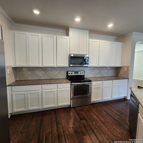 a kitchen with granite countertop white cabinets a sink and dishwasher a stove with wooden floors