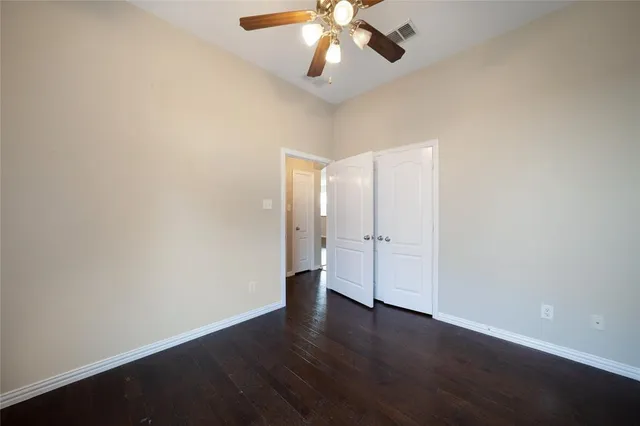 an empty room with wooden floor chandelier fan and windows