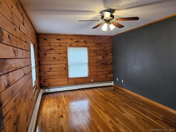 a view of an empty room with wooden floor and a chandelier fan