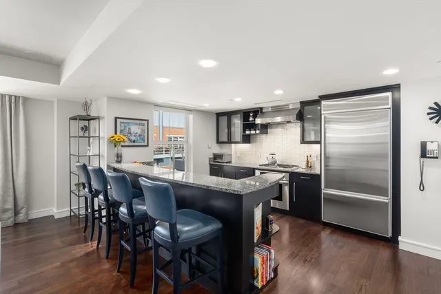 a kitchen with stainless steel appliances granite countertop a dining table chairs refrigerator and wooden floor