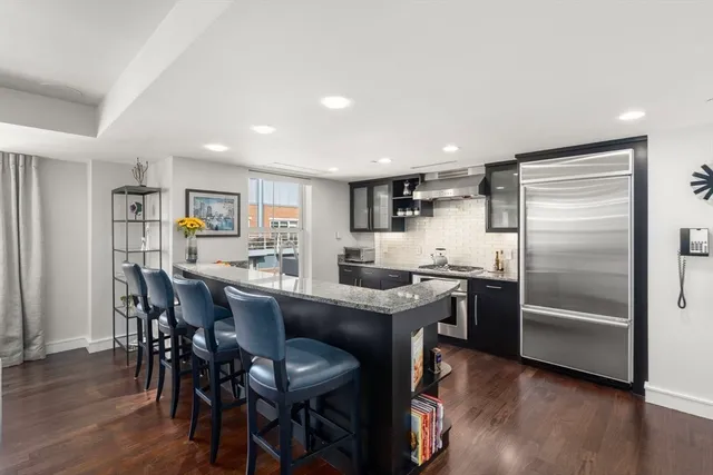 a kitchen with stainless steel appliances granite countertop a dining table chairs refrigerator and wooden floor