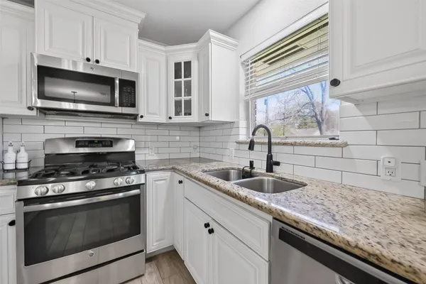 a kitchen with stainless steel appliances granite countertop a stove a sink dishwasher a refrigerator and white cabinets with wooden floor