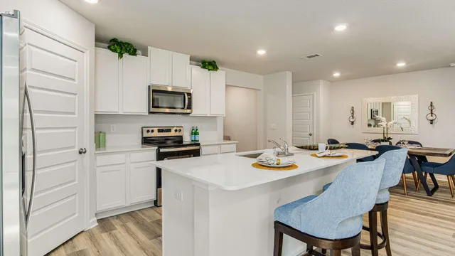 a kitchen with stainless steel appliances granite countertop a stove a sink a microwave a refrigerator and white cabinets with wooden floor