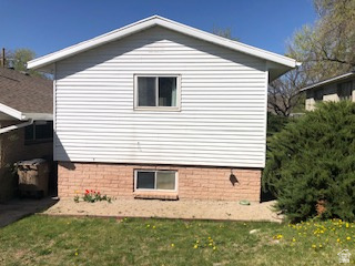 1615 Pioneer Road Draper, UT 84020 - Photo 13 of 13 White siding exterior with a pitched roof, featuring brick foundation accents, a ground-level window, and a mature evergreen shrub