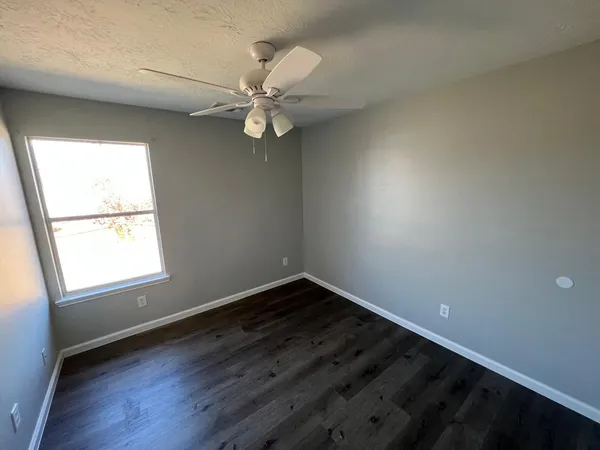 an empty room with wooden floor fan and windows