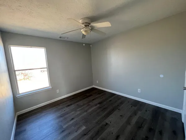 an empty room with wooden floor fan and windows