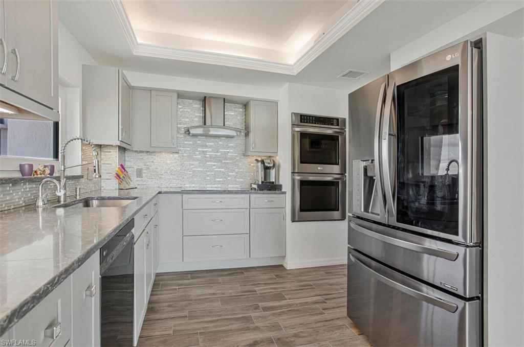 4031 Gulf Shore Boulevard North, Unit 6B Naples, FL 34103 - Photo 10 of 37 Kitchen featuring stainless steel appliances, a tray ceiling, wood finish floors, and light stone counters