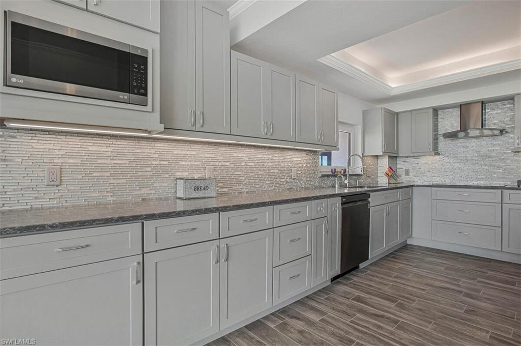 4031 Gulf Shore Boulevard North, Unit 6B Naples, FL 34103 - Photo 9 of 37 Kitchen with dark stone countertops, stainless steel microwave, wood finish floors, crown molding, and wall chimney exhaust hood