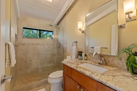 a bathroom with a granite countertop sink a toilet a mirror and shower