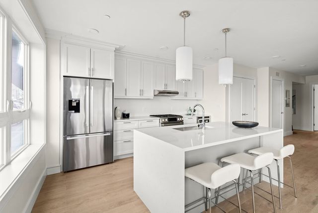 a kitchen with stainless steel appliances kitchen island granite countertop a refrigerator a sink a stove and white cabinets with wooden floor