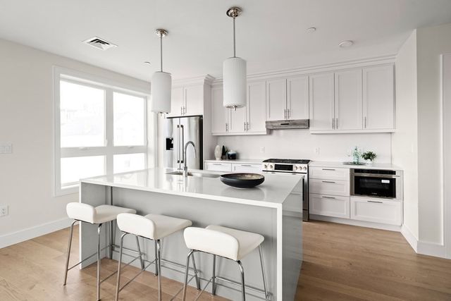 a kitchen with stainless steel appliances granite countertop a stove a sink a refrigerator and white cabinets with wooden floor